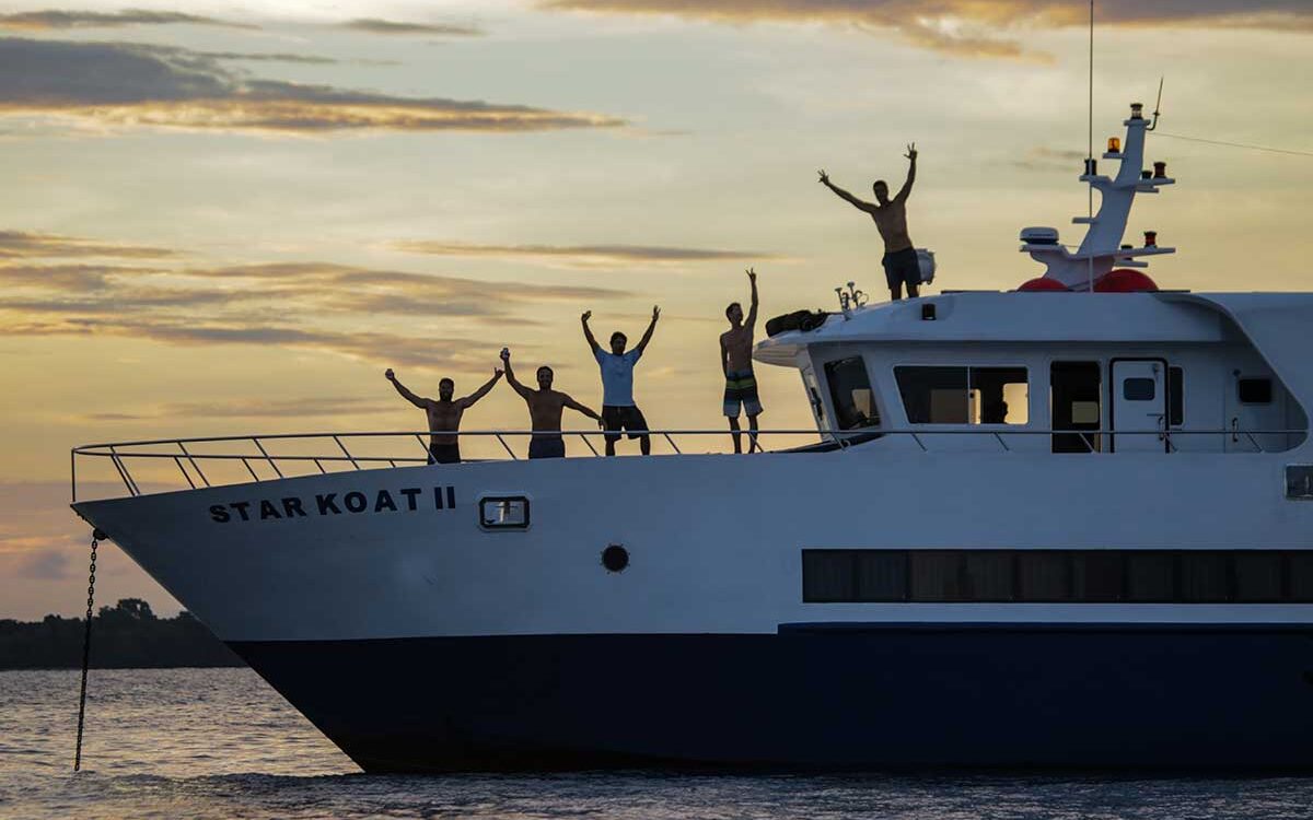 Surfers celebrating on the Star Koat 2 surf charter boat in the Mentawai Islands at sunset